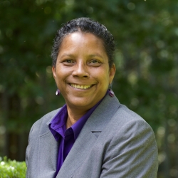 head shot of Archene Turner, Community Minister at Cedar Lane in the courtyard with greenery behind her